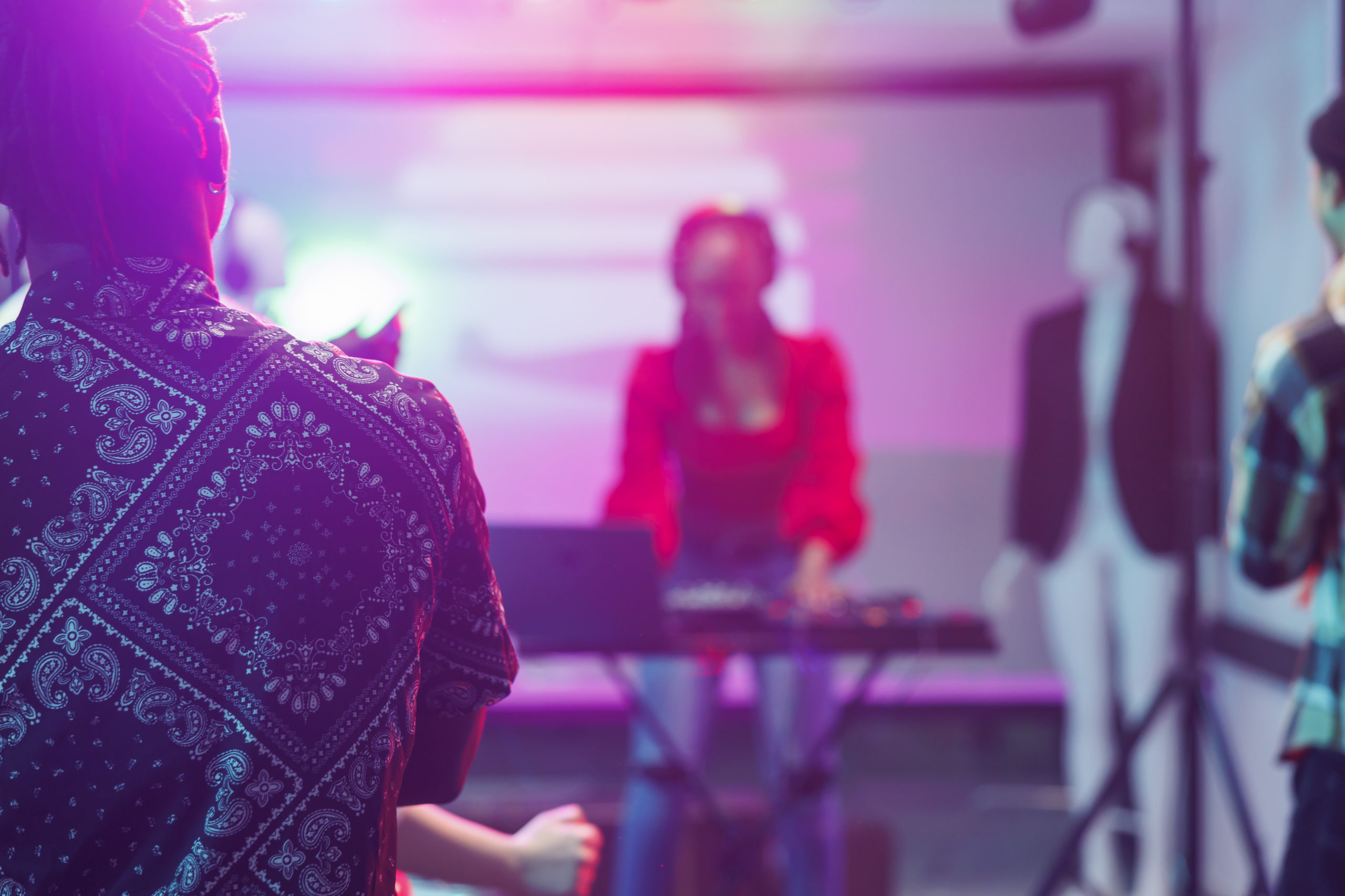 People watching live electronic music concert on stage with spotlights in nightclub. African american musician performing using dj controller in nightclub on blurred background